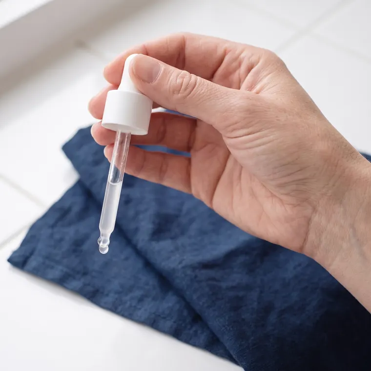 Serumpipet met druppel in een hand boven indigoblauw linnen